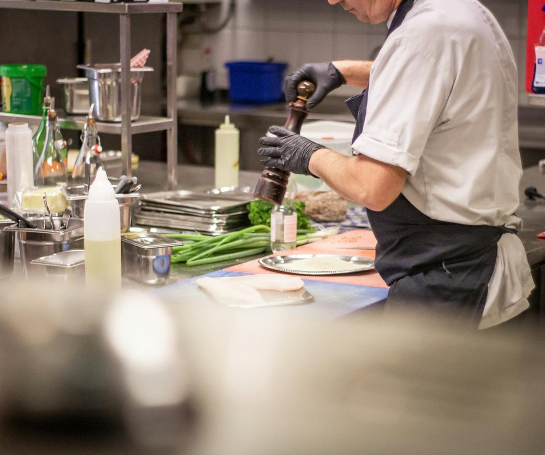 A cook in gloves seasoning a dish on the line